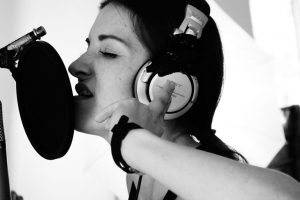 Dark haired girl singing into studio microphone wearing headphones